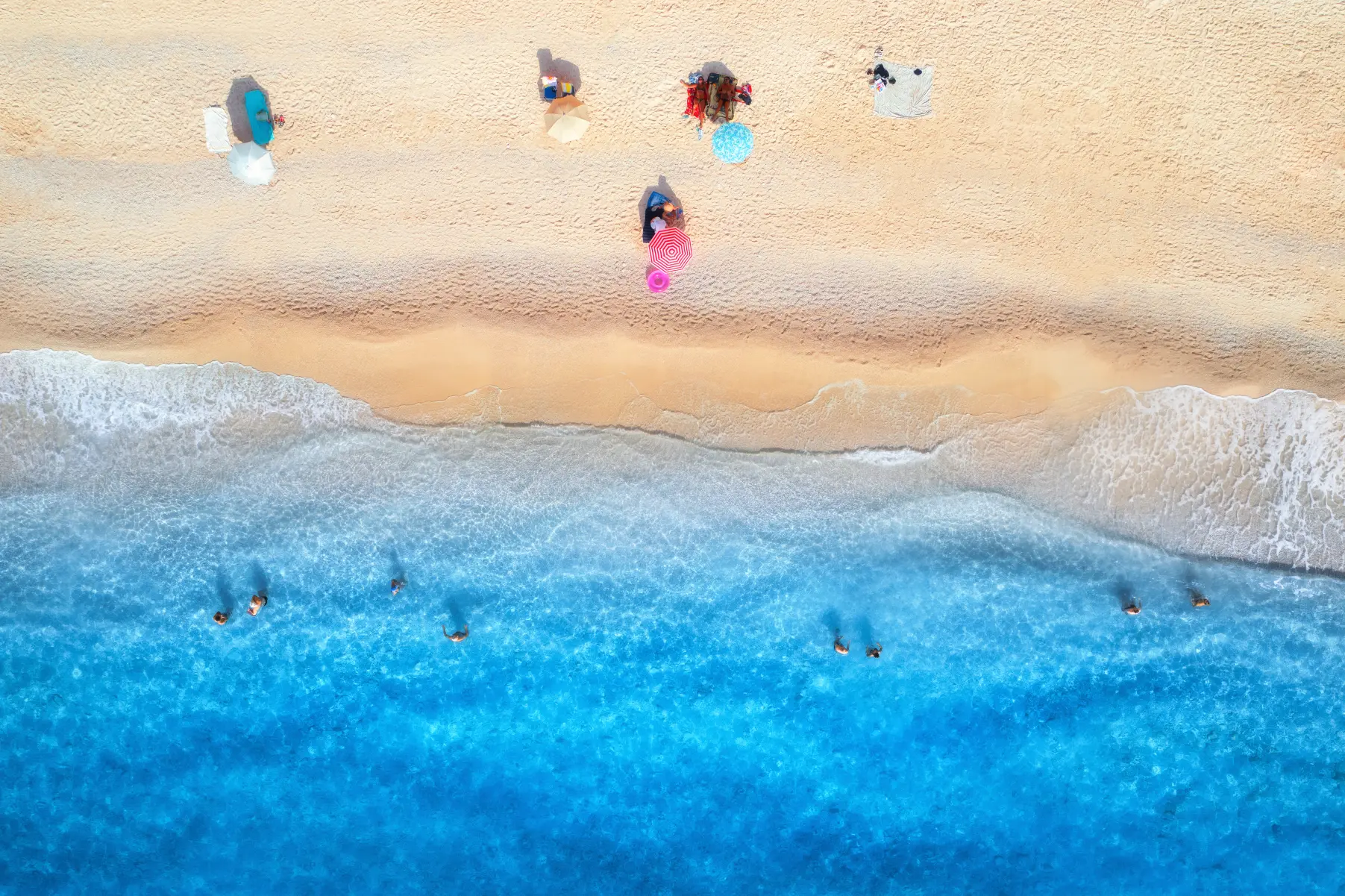 Top-down drone view of beach with colorful umbrellas and swimmers
