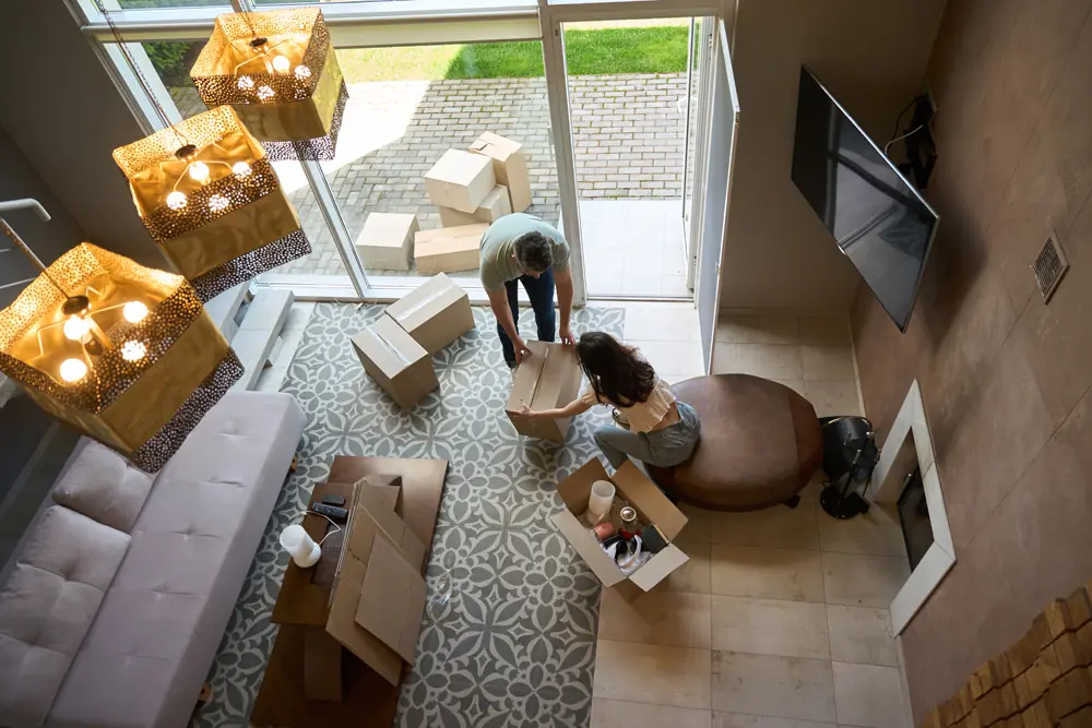 Couple packing moving boxes in a modern living room with open door and stacked cardboard boxes near entryway