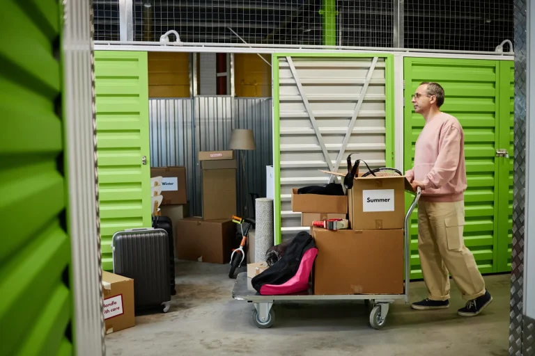 Man pushing trolley with stacked boxes in green storage corridor.
