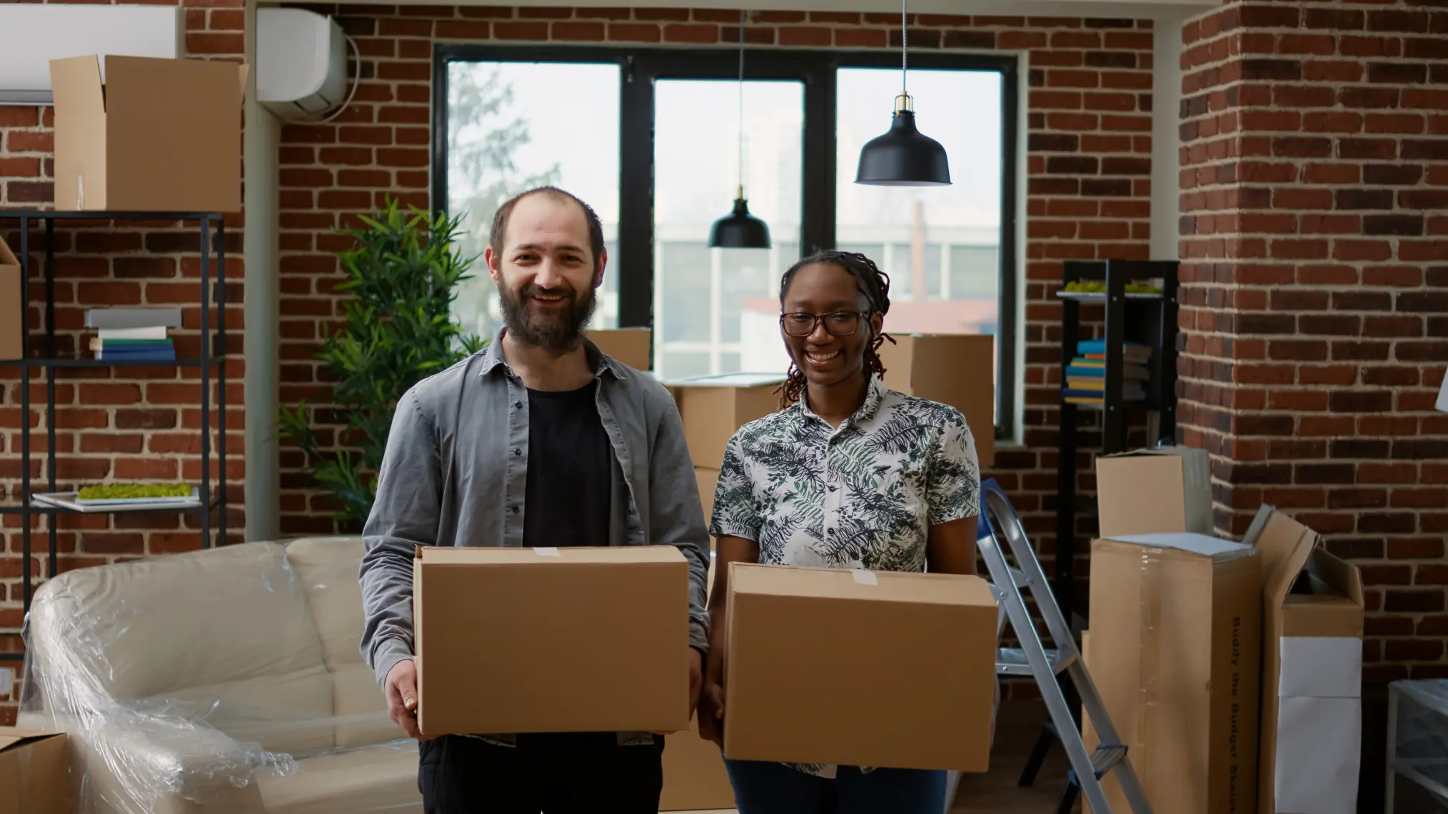 Couple packing moving boxes in a modern living room with open door and stacked cardboard boxes near entryway