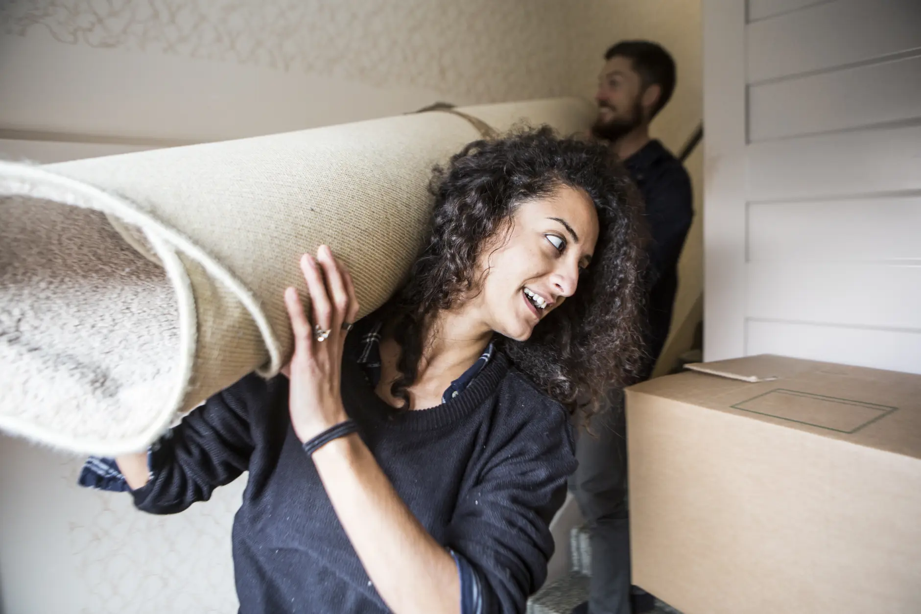Couple packing moving boxes in a modern living room with open door and stacked cardboard boxes near entryway