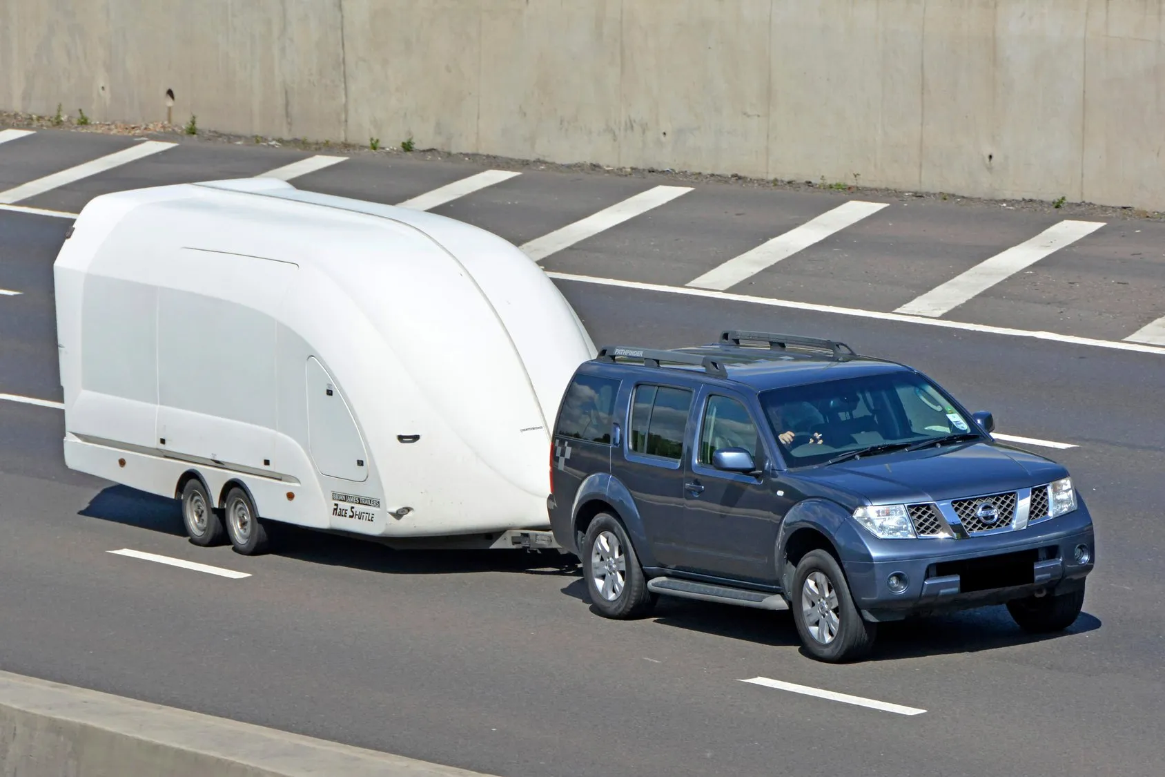 Blue SUV pulling white enclosed car carrier down highway
